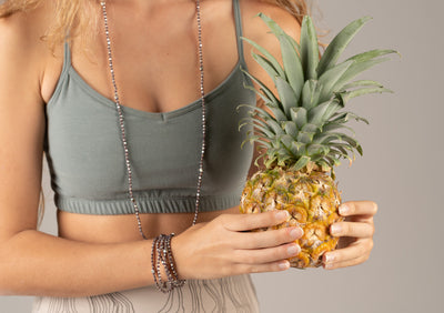 A woman holding pineapple wearing purple and brass necklace and bracelets.