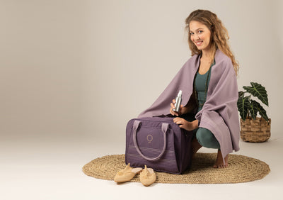 young woman holding a purple fitness bag, a yoga spray and wearing a lavender wrap. 